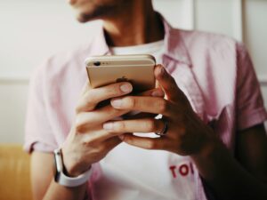 ピンク色のシャツを着た男性がスマホを持っている